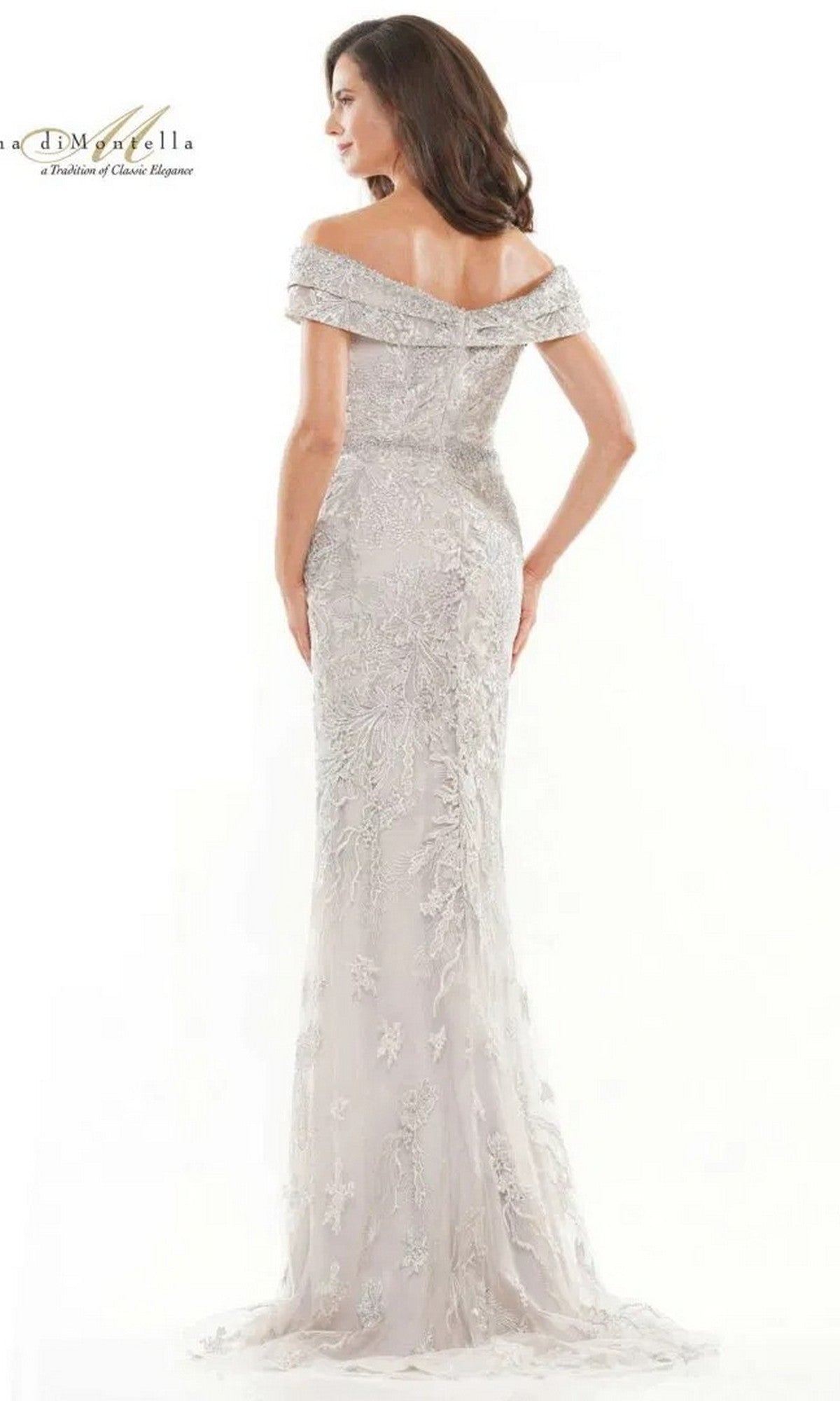 A woman stands with her back to the camera in a silver, floor-length Rina Di Montella RD2737 formal dress featuring off-the-shoulder sheer lace, floral embroidery, and a beaded waist, set against a white background.